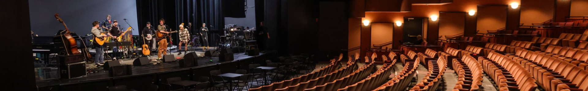 Musicians rehearsing on stage in the Joan C. Edwards Performing Arts Center with auditorium seating in the foreground.